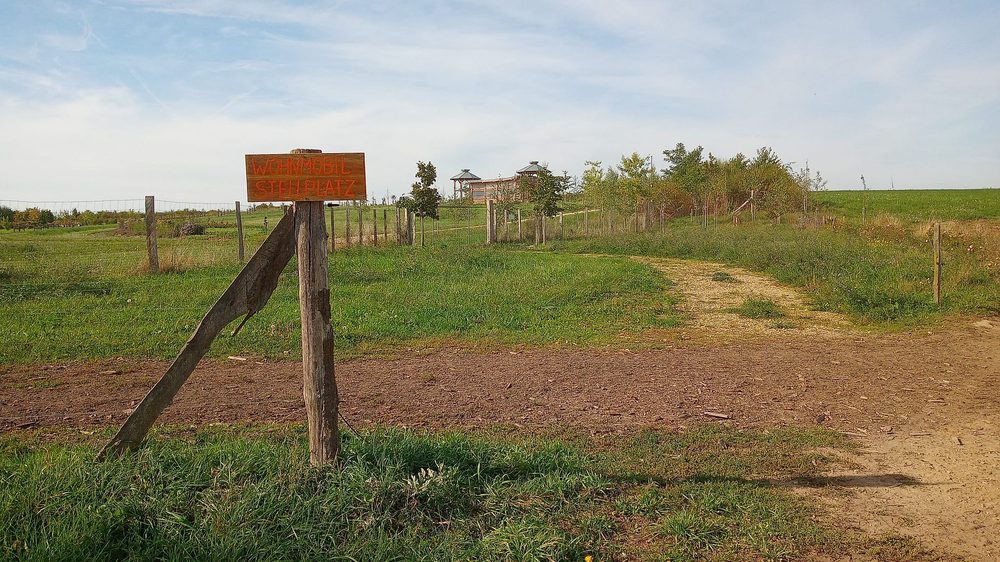 Stellplatz für Wohnmobile auf Hofgut Pulsitz, ausgeschildert mit einem Holzschild, dahinter Wiese und Weg