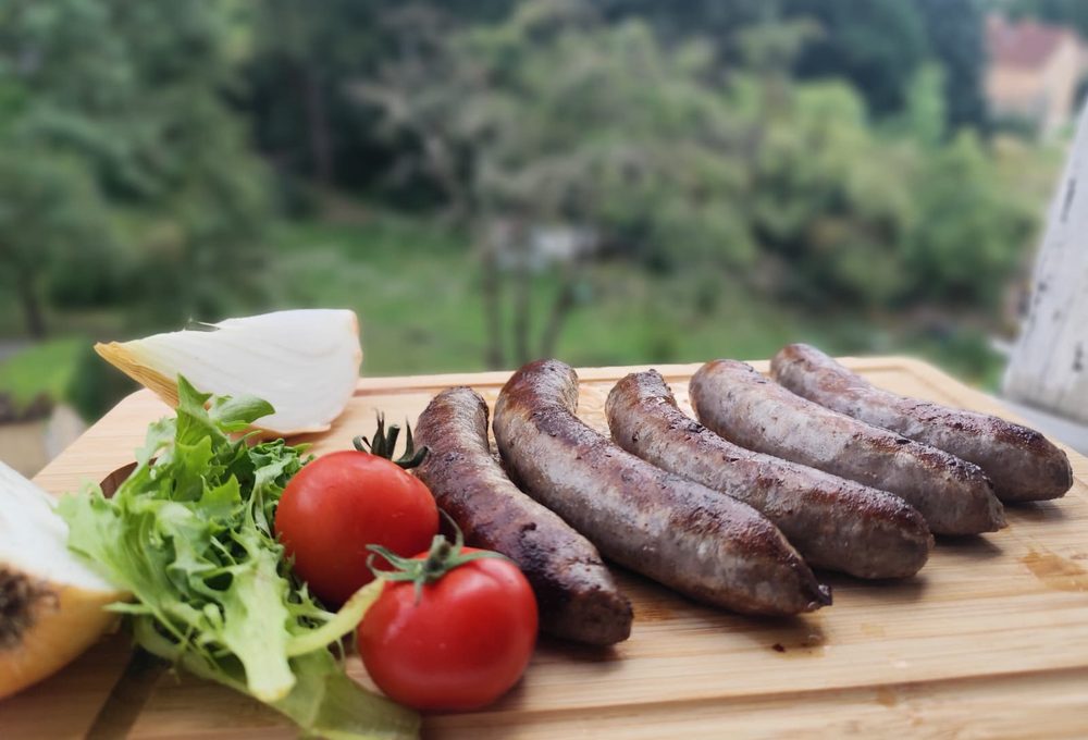 Gegrillte Bratwürste vom hofeigenen Rind auf einem Holzbrett mit Tomaten und Salat