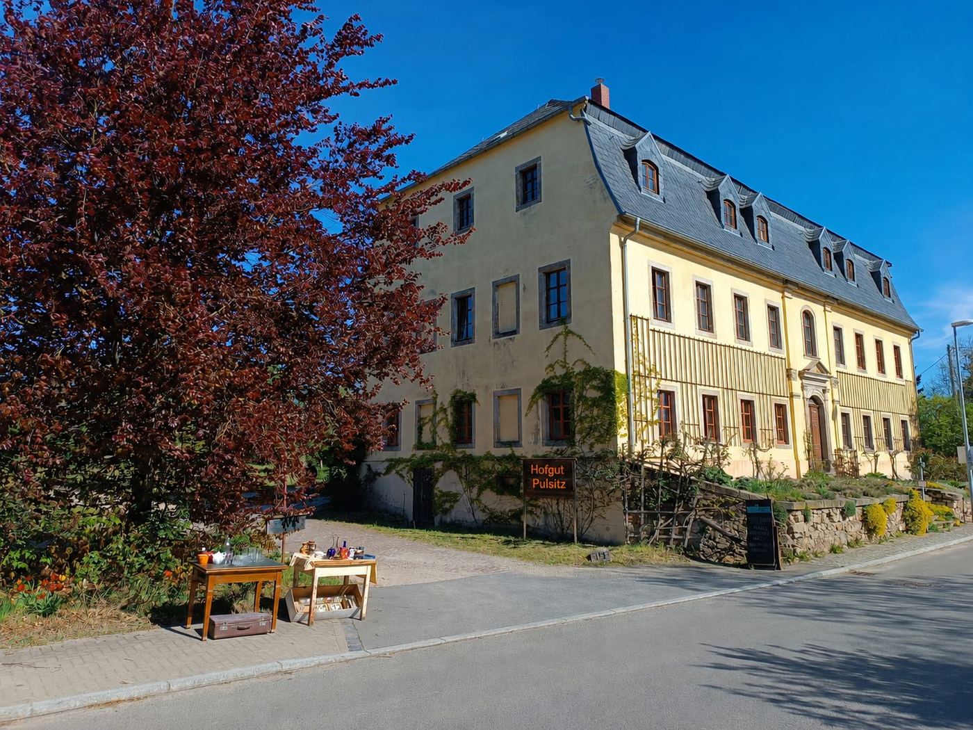 Hofeinfahrt von Hofgut Pulsitz mit Herrenhaus, Bäumen und Hofladen-Schild